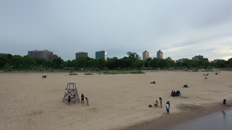 Video-Aéreo-Que-Se-Aleja-De-La-Playa-Monrose-En-Chicago,-Que-Muestra-A-La-Gente-Jugando-En-La-Playa-Y-La-Ciudad-Al-Fondo