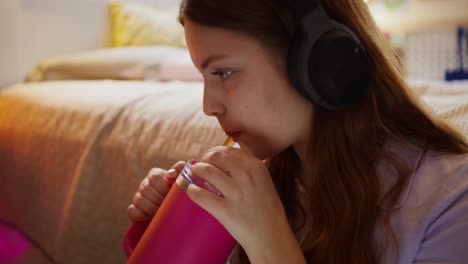 una adolescente escuchando música y bebiendo una bebida rosa
