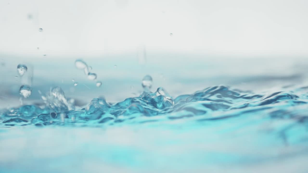슬로우 모션의 깨끗한 물 표면은 물이 튀는 상점으로 화면을 채우고 기포로 액체 표면을 흔들고 있습니다.