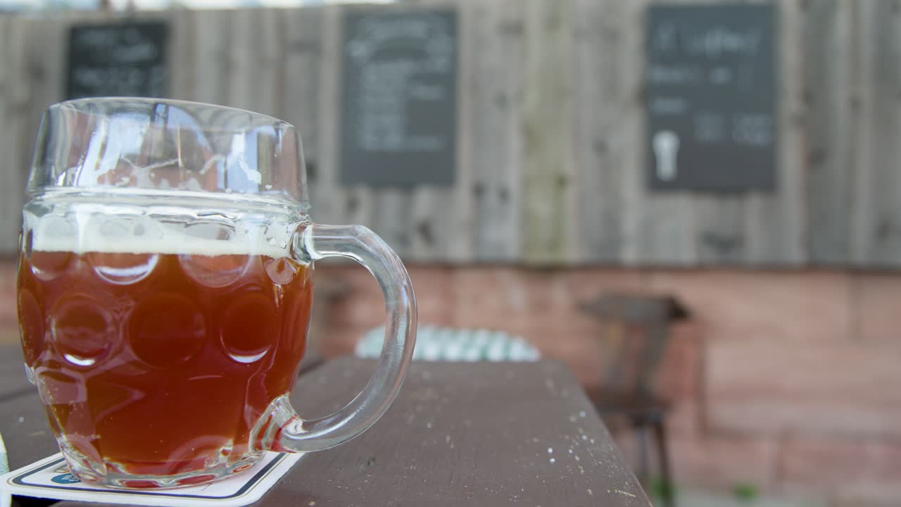 Two glass beer mugs with amber ale on wooden table, outdoor beer garden, natural daylight