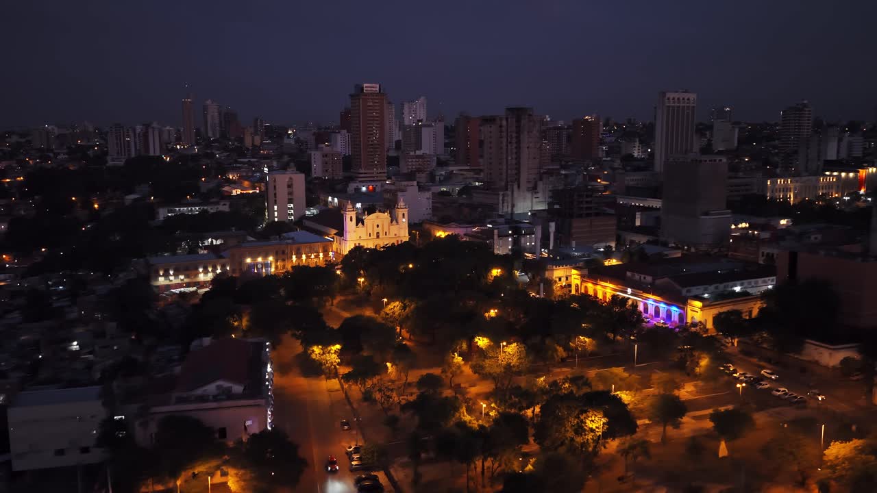 Plaza de la Independencia with trees and streetlights surrounded by cathedral, university, and illuminated buildings, Asunción at night