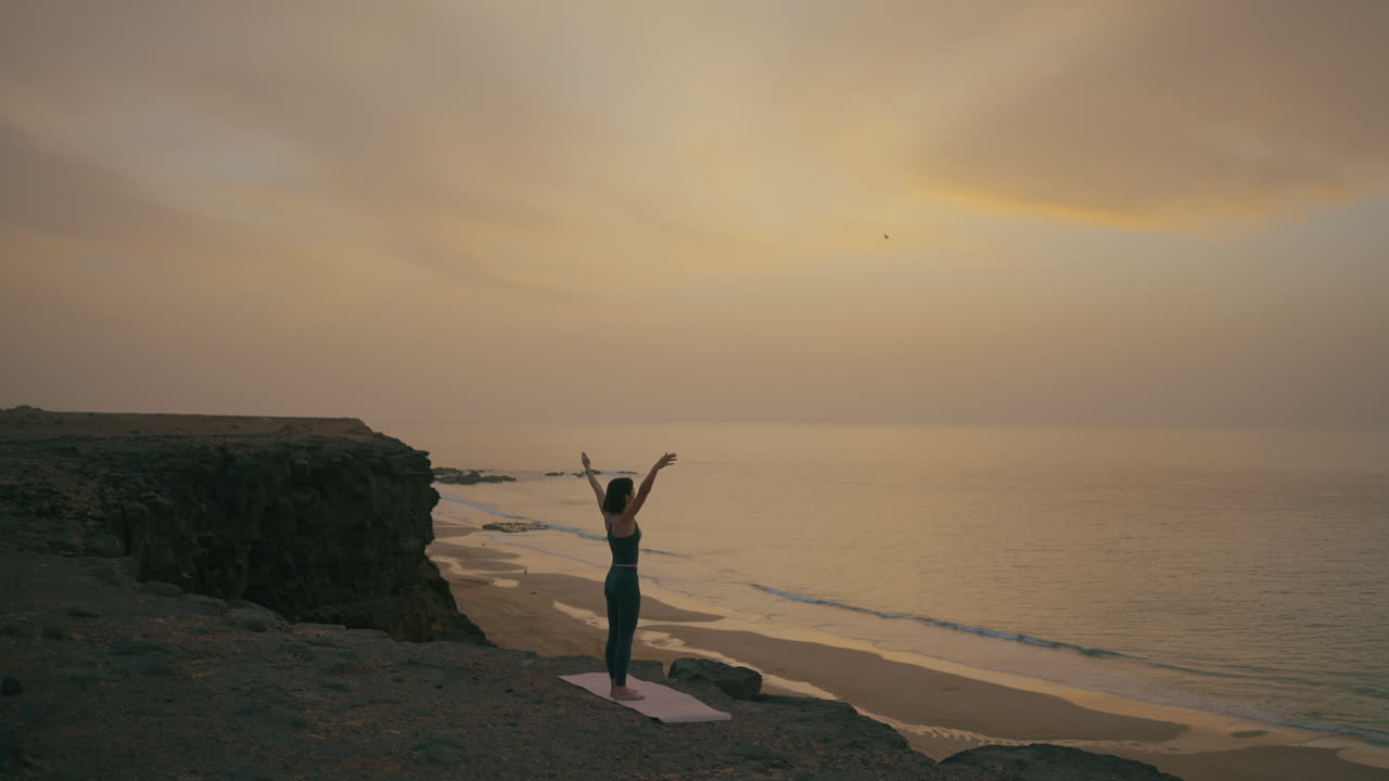 Woman practicing yoga at sunset over the ocean
