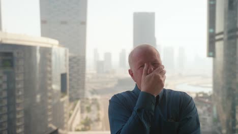 senior man presses record on his camera then poses with different emotions for a social media video thumbnail with a cityscape in the background