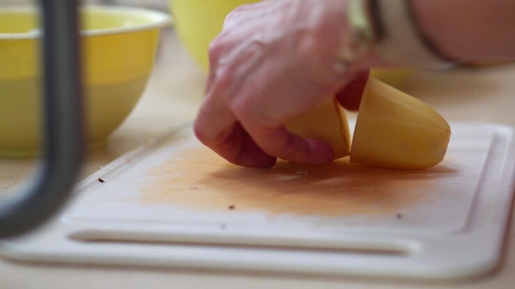 Mani femminili che tagliano patate fresche pelate su un tagliere. Primo piano, vista laterale.