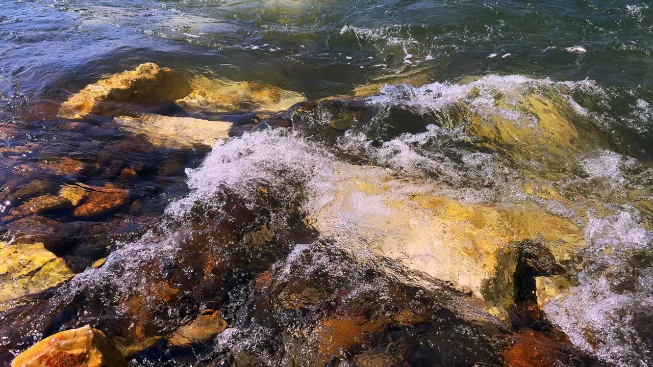 A Serene Encounter with Nature: Waves Gently Lapping Against the Colorful Rocks by the Water's Edge Captured in Vivid Detail