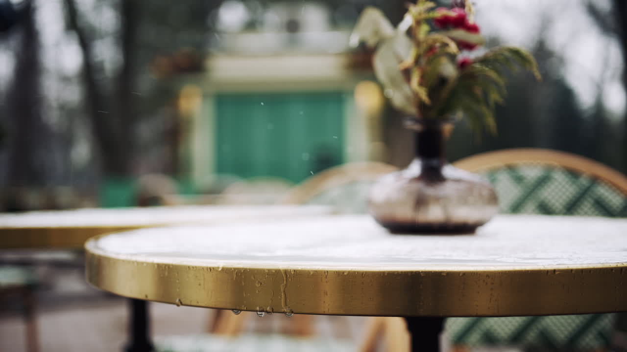 Piccolo vaso decorativo in vetro con bacche invernali e verde su un tavolo da esterno con luci festive sullo sfondo