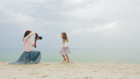 young photographer mother taking photo of daughter on beach