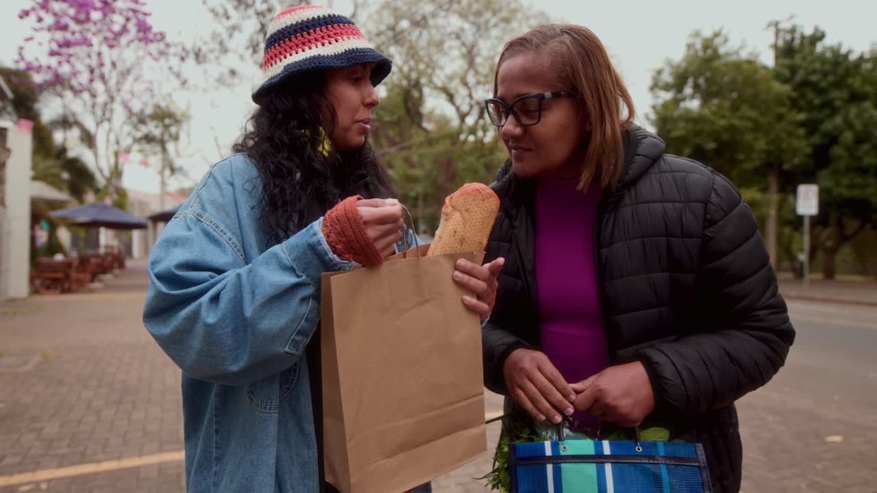 Two women with groceries and a baguette outdoors