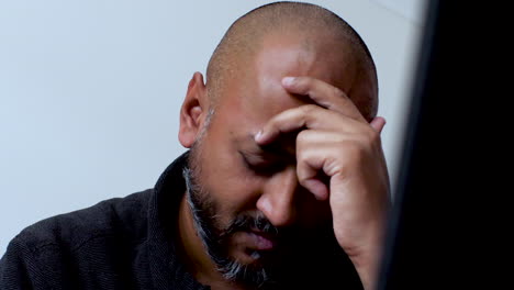 south asian man feeling tension and anxiety, rubbing his forehead in a moment of stress and helplessness