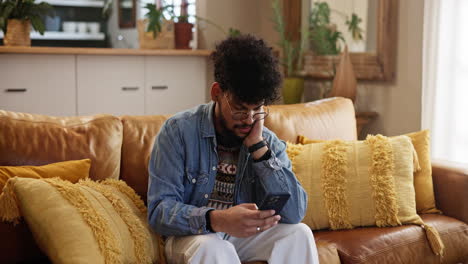 a man looking down at his phone, sitting on a couch