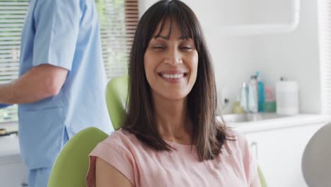 portrait of smiling biracial female patient looking at camera at modern dental clinic