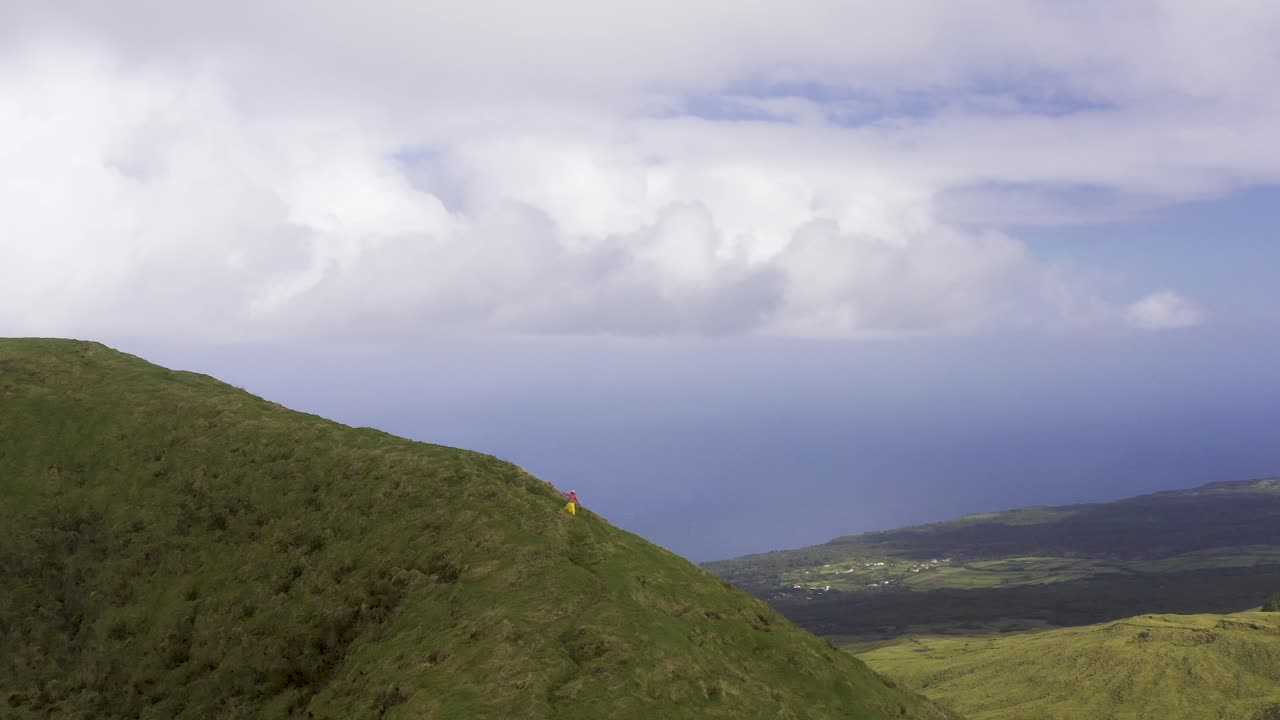 Mulher turista asiática gravando vídeo com celular em um caminho na encosta da montanha vulcânica exuberante e verde, vista de drone do Pico da Esperança, na ilha de São Jorge, nos Açores, Portugal.