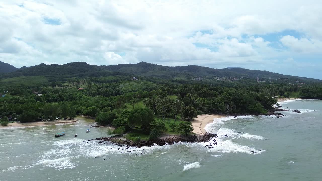 Aerial drone footage of Koh Lanta in Thailand showing longtail boats anchored by the shore, lush palm trees, tropical forest and rocky coastline with scenic turquoise sea