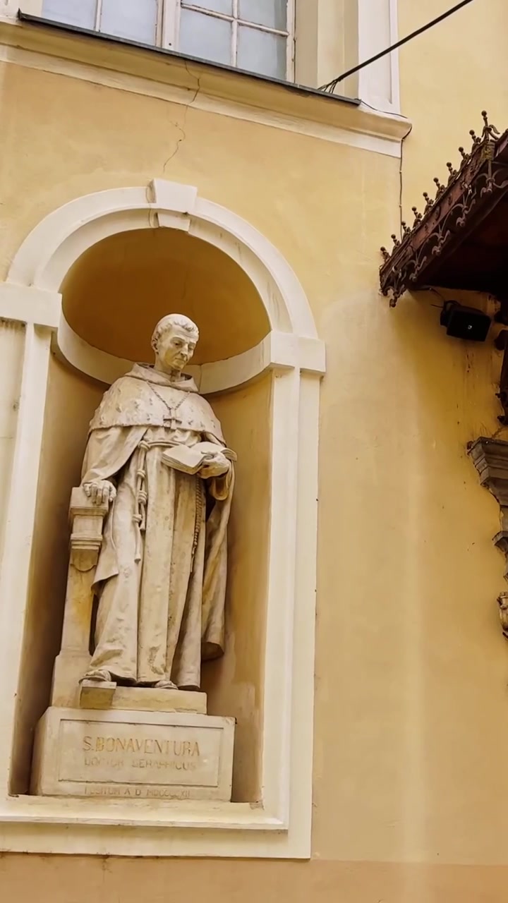 Vista verticale dell'ingresso ornato della Cattedrale di Lubiana, con statue di San Bonaventura e Tommaso d'Aquino, una porta di bronzo scolpita e una tettoia decorativa in metallo.