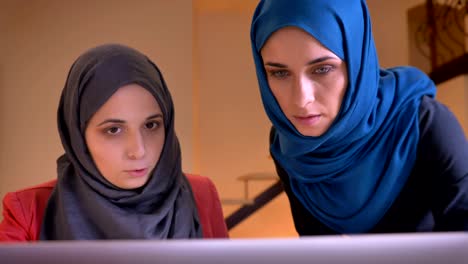 closeup shoot of two young muslim female office workers in hijabs discussing the data on the laptop. boss instructing a younger employee