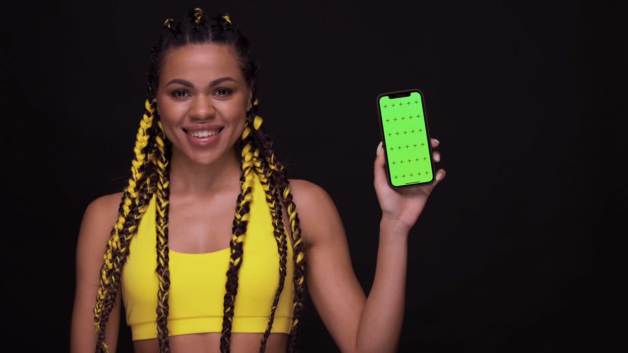 retrato de una chica afroamericana sonriente apuntando con el dedo a la pantalla del teléfono móvil con una llave cromática. mujer aislada sobre un fondo negro