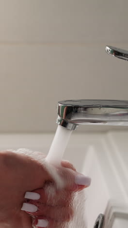 woman opens faucet and washes hands over white sink with clean running water slow motion. hygienic procedures in home bathroom. lady cleans skin of hands