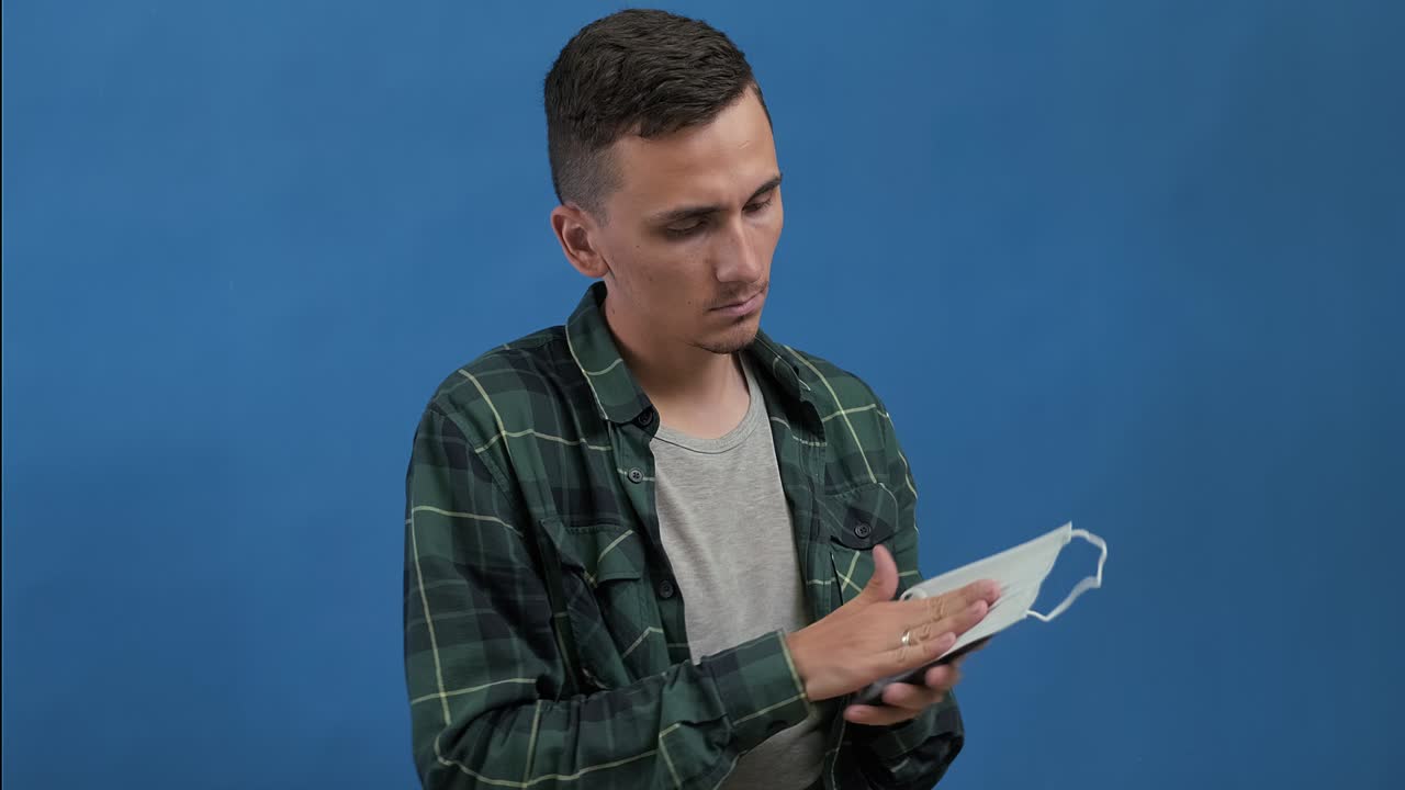 el hombre se sienta, usa el teléfono, luego limpia su pantalla con una máscara médica y la desecha.