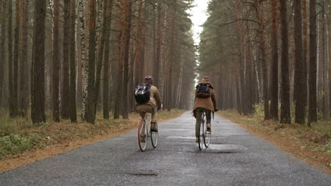 rear view of a couple wearing winter clothes riding bikes in the forest while raining