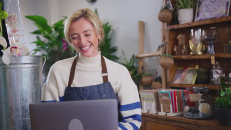 Female-Owner-Of-Florists-Shop-Using-Laptop-Computer-For-Video-Call-Showing-Bunch-Of-Flowers