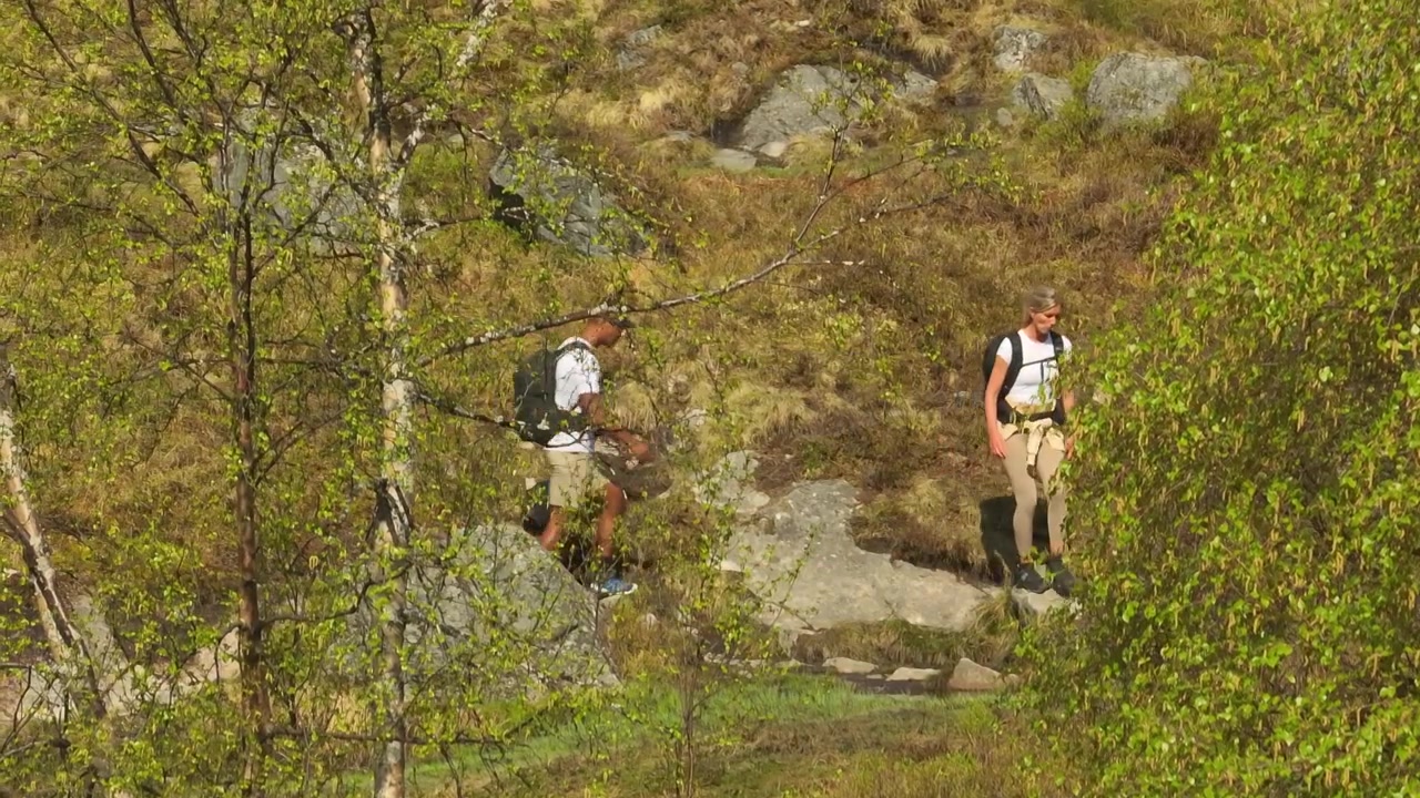 Filmato ravvicinato con drone di una coppia in escursione su grossi macigni, circondata da alberi e arbusti, in un paesaggio selvaggio e aspro durante un'avventura all'aria aperta in Norvegia.