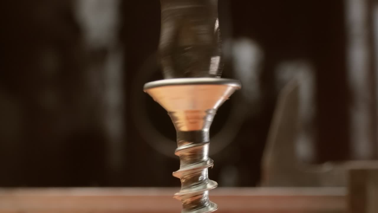 el primer plano es un taladro eléctrico que atornilla un tornillo automático en una barra de madera.