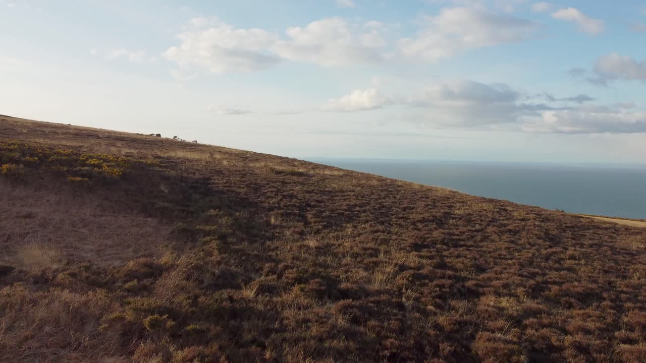 disparo de seguimiento aéreo al atardecer sobre páramos con un hermoso cielo azul y un hermoso mar en north devon, reino unido
