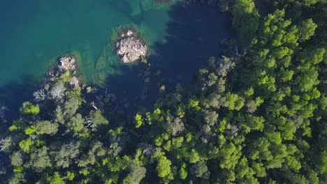 Aerial-drone-shot-of-a-lake-bay-with-trees,-rocks-and-emerald-water