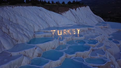 the illuminated turkey sign is reflecting in the turquoise travertine pools of pamukkale at dusk, creating a magical atmosphere in this unique natural wonder of turkey