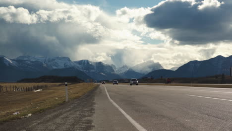 Several-vehicles-drive-past-camera-on-freeway-with-beautiful-mountains-in-the-background-and-some-garbage-on-the-side-of-the-road