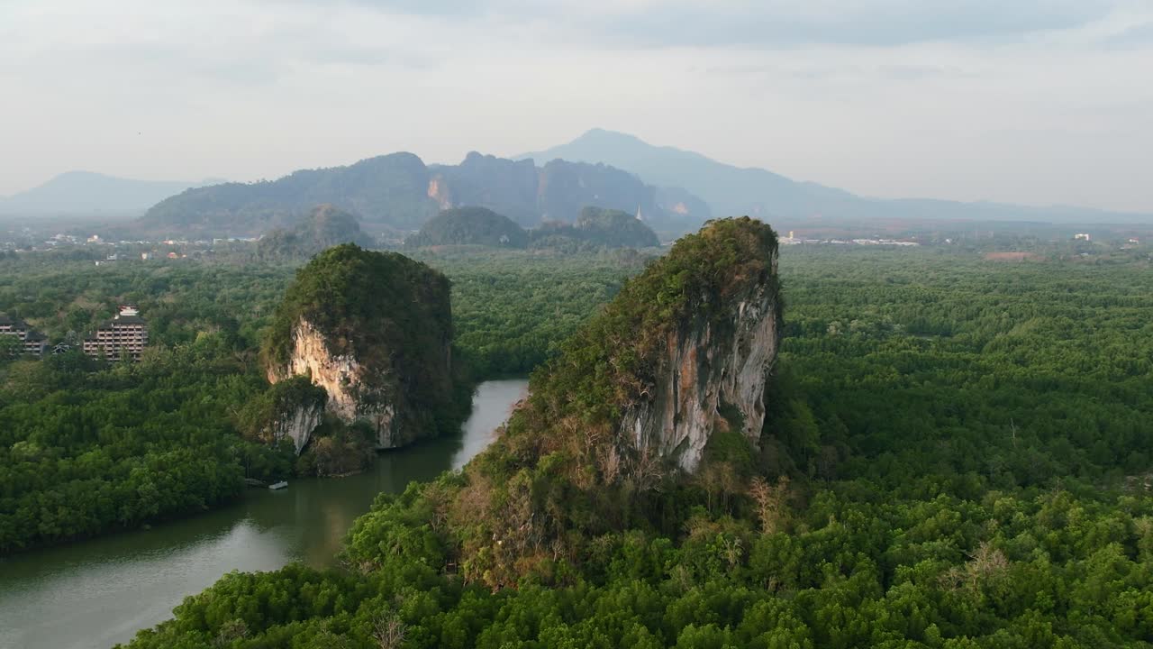 Cảnh quay drone lia máy từ trên không của những ngọn núi đá vôi xanh lớn với một dòng sông ngập mặn chảy qua giữa chúng vào một buổi chiều hoàng hôn ở thị trấn Krabi, Thái Lan