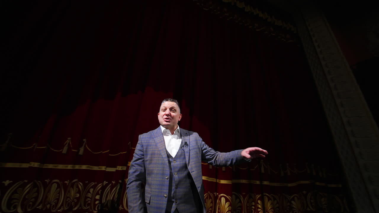 Senior male entertainer dances on stage in front of theater hall. Speaker akes audience laugh. Entertainment concept.