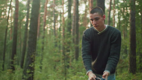 young man in casual sweater opens tent fabric in forest clearing as soft natural sunlight creates glowing atmosphere among trees during quiet moment of outdoor setup in serene woodland environment