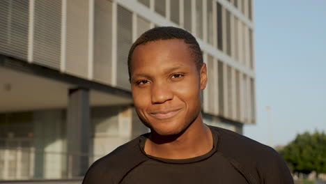 retrato de un joven negro alegre sonriendo y mirando a la cámara al aire libre. hermoso atleta afroamericano descansando en una tarde soleada. primer plano.