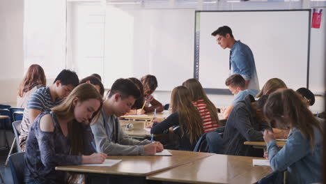 maestro de secundaria caminando entre los escritorios mientras los estudiantes trabajan durante la lección