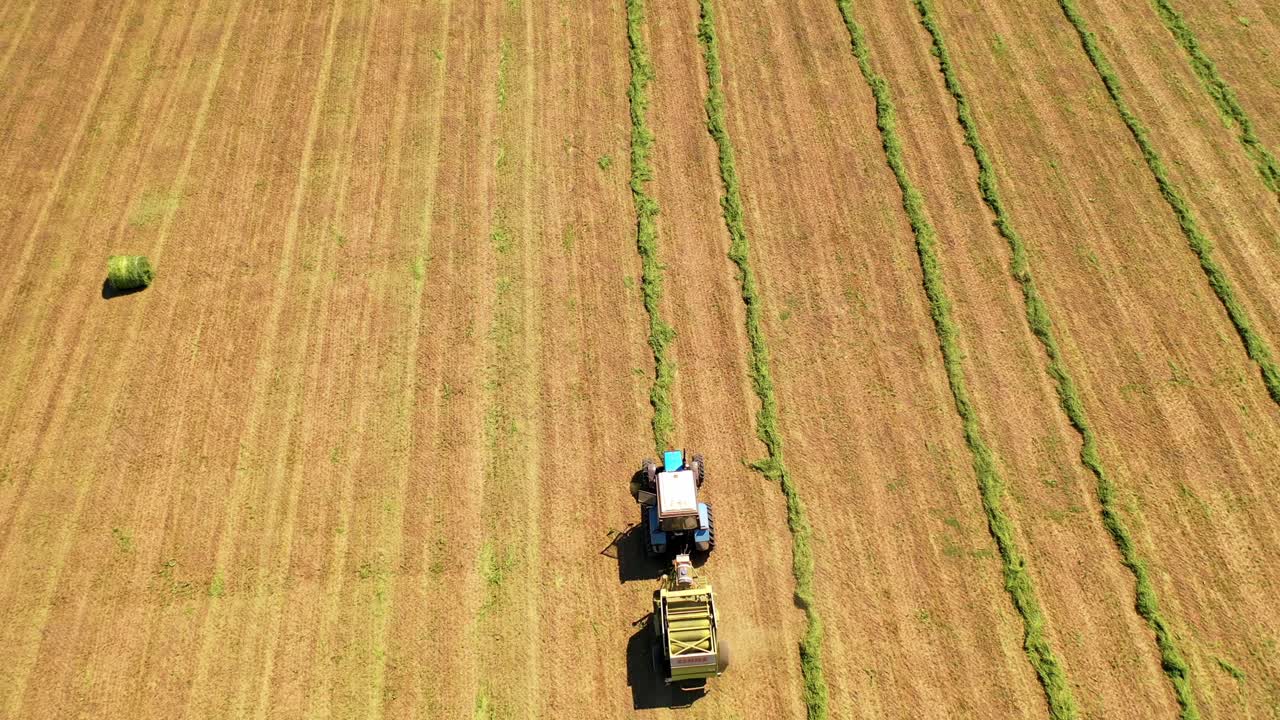 Drone view of agricultural machine working on the field. Tractor collects dried grass for feeding livestock. Motion camera bottom up.
