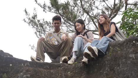young asian indonesian friends chatting and laughing on rocky hilltop in nature