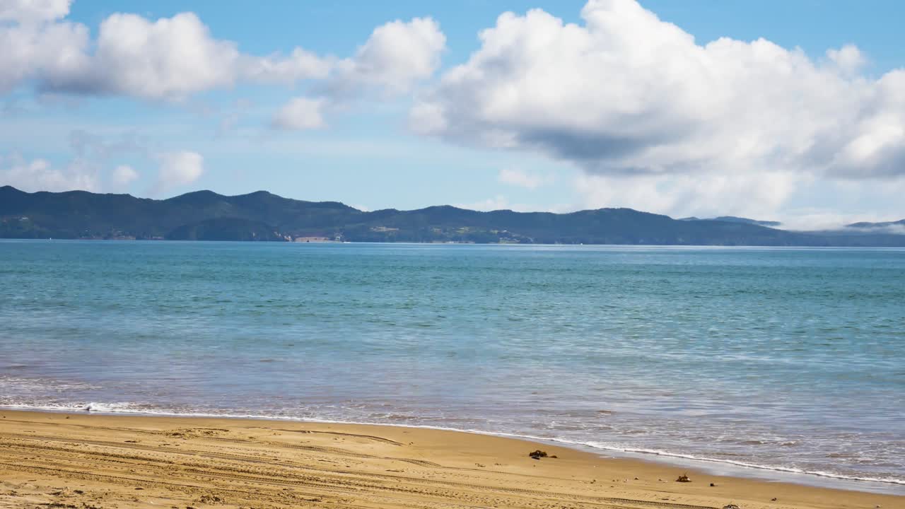뉴질랜드의 화창한 날과 흐린 날에 모래 해변에 물이 닿는 열대 마이타이 만 - 해안에 사람이 없음 - 패닝 샷