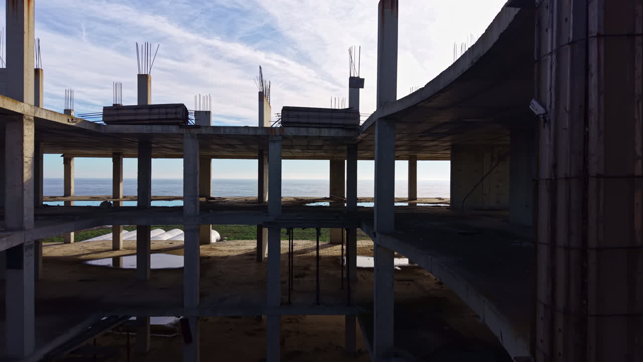 Vasta distesa marina vista attraverso pilastri di cemento in una struttura abbandonata in riva al mare durante l'ora d'oro