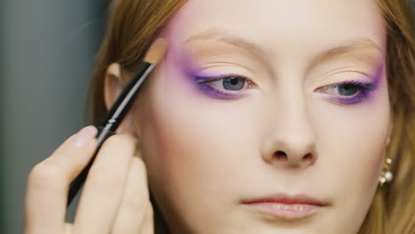 a young blue-eyed woman is applied make-up on her face