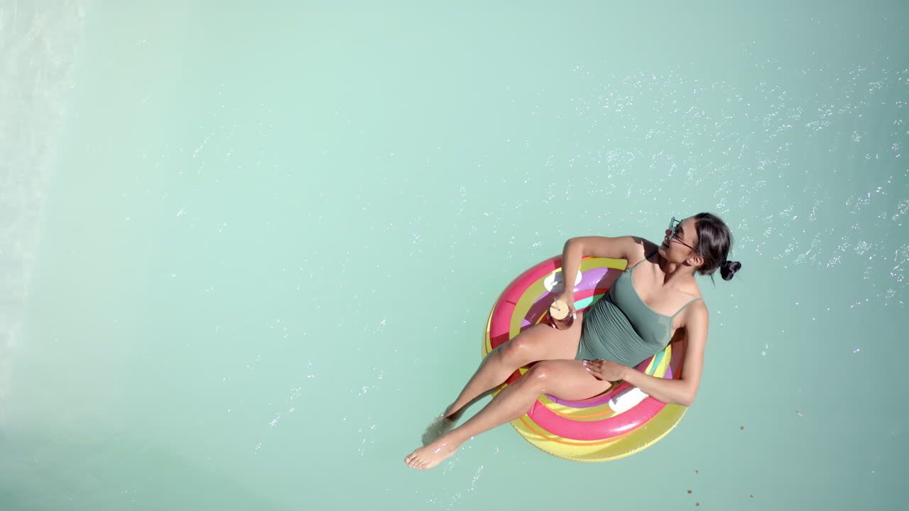 Relaxing in pool, woman on inflatable ring enjoying drink in swimsuit, copy space
