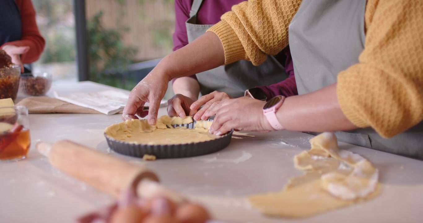 Diverse female bakers pressing crimping tart crust from pastry at counter in fluted pan for baking