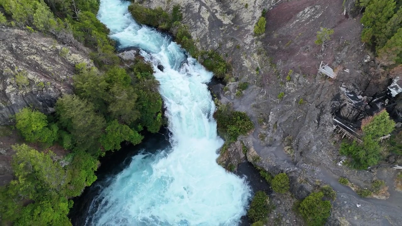 Dron stoupá nad řekou Truful Truful v národním parku Conguillio, odhaluje bělostné peřeje protékající hlubokým kaňonem s tmavými lávovými útvary a hustým zeleným lesem.