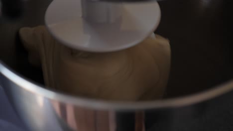 macro shot of dough being beaten on white kitchen aid mixing hook in large silver bowl