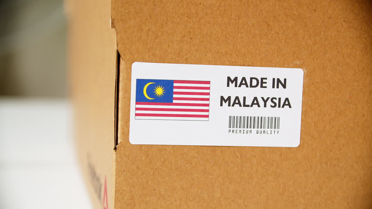 Hands applying MADE IN MALAYSIA flag label on a shipping cardboard box with products
