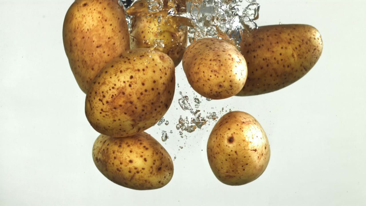 Diverse patate fresche che schizzano nell'acqua su sfondo bianco