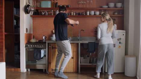 Feliz-Pareja-Joven-Bailando-En-La-Cocina-Disfrutando-De-Un-Divertido-Baile-Juntos-Divirtiéndose-Celebrando-La-Relación-El-Fin-De-Semana-En-Casa