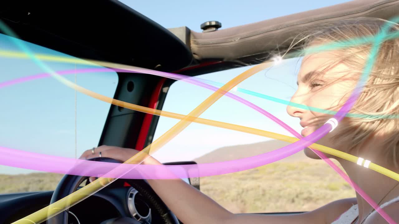 Donna che guida un'auto, con il vento dal tetto che fa incrociare nastri sul viso, che tiene il volante e sorride per la brezza.