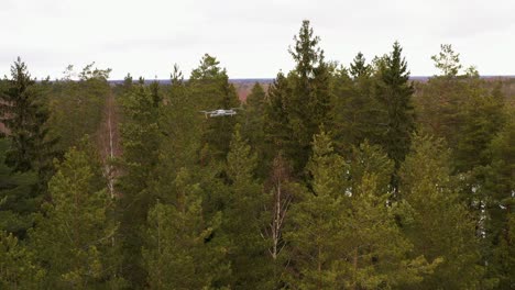 Drone-shot-of-another-drone-flying-above-snowy-forest-in-rural-area