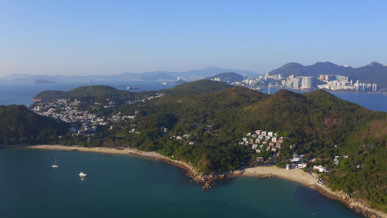 화창한 날 산과 숲 사이에 마을과 해변이 있는 열대 섬 위로 앞으로 이동하는 드론 샷